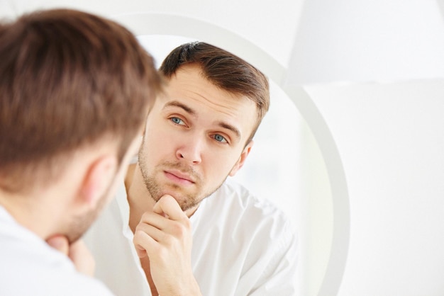 Young attractive Caucasian man examines his face in the mirror closeup Aging concept forehead wrinkles