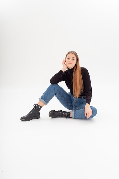 Young attractive caucasian woman in black turtleneck, blue jeans at white studio