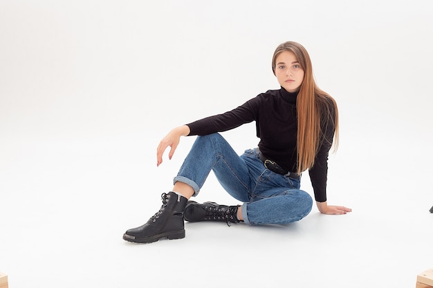 Young attractive caucasian woman in black turtleneck, blue jeans at white studio