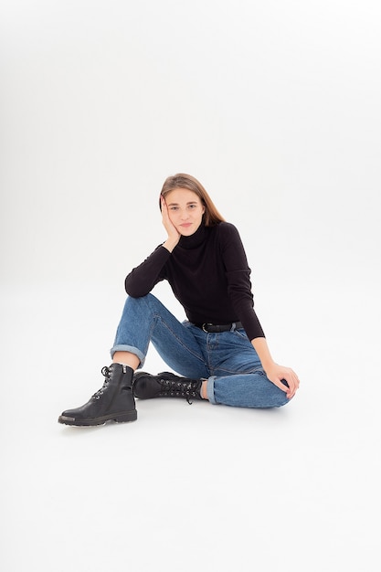 Young attractive caucasian woman in black turtleneck, blue jeans at white studio