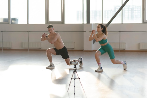 Young attractive couple boy and girl exercising in gym recording video blogging about sports