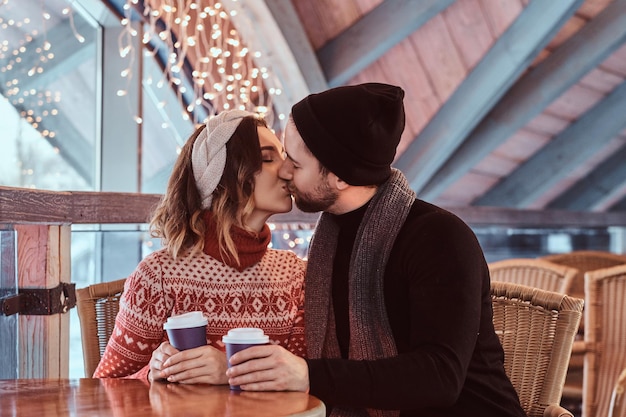 Young attractive couple on a date in an ice skating rink, kiss while sitting at the table in the hall