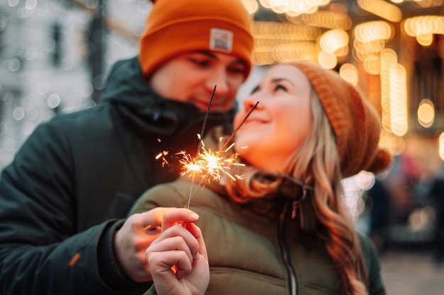 Young attractive couple hug and kiss outdoors with the sparklers in their hands celebrating New Year