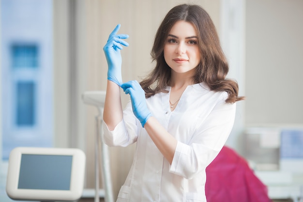 Young attractive doctor female indoors. Portrait of woman wearing medical uniform in the clinic. Doctor with medical equipment. Cosmetologist in her parlor