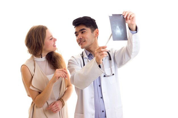 Young attractive doctor with black hair in gown with stethoscope showing Xray to young sad woman