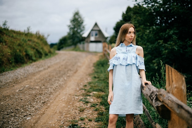 Young attractive elegant blonde girl in blue romantic dress posing on the road in the countryside