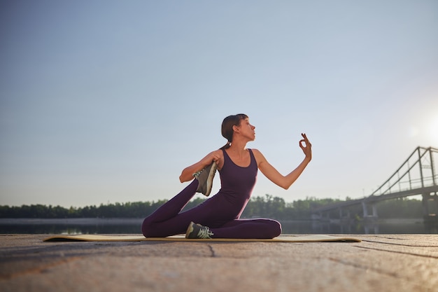 young attractive female is doing morning yoga exercises at city near river