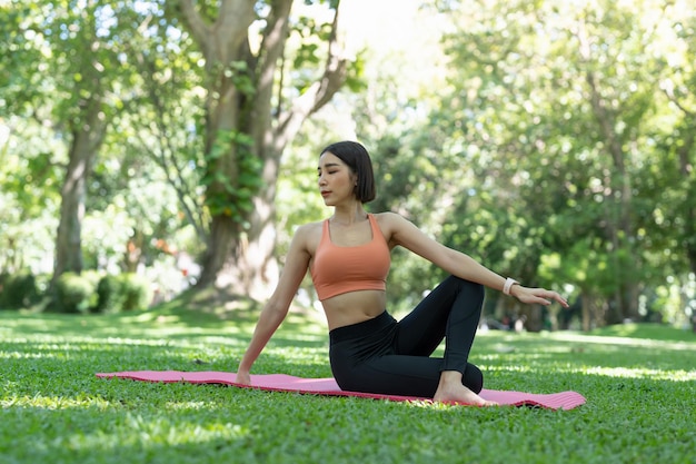 Young attractive girl is doing advanced yoga asana on the fitness mat in the middle of a park