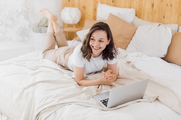 A young attractive girl is lying in bed and checking social networks modern bright apartment