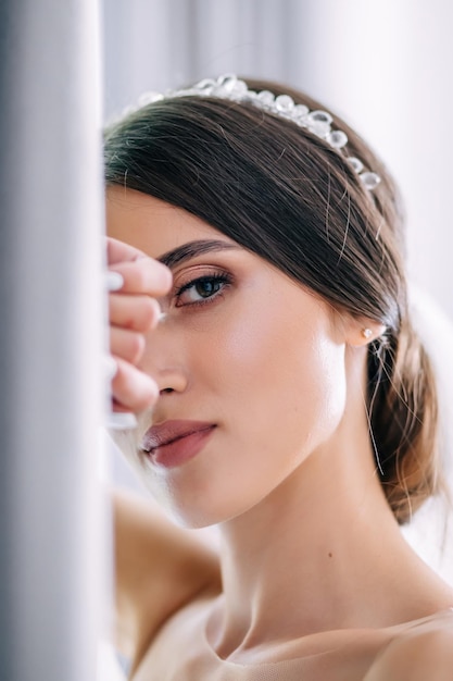 Photo young attractive girl looks at the camera and puts her hand on half of her face delicate bride with hair and makeup is preparing for the wedding