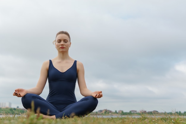 Young attractive girl practicing yoga sitting in half lotus exercise ardha padmasana pose