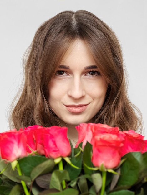 Young attractive girl with a bouquet of red roses on a white background close up A happy girl with a bouquet of roses is smiling The concept of happiness joy and celebration