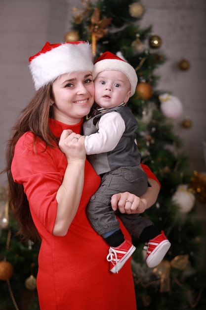 Young attractive happy mother in santa's hat have a good time with her son at home near christmas tree. Family, happiness, holidays, new year concept