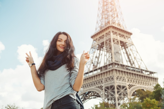 Young attractive happy woman showing peace gesture Eiffel Tower in Paris, France