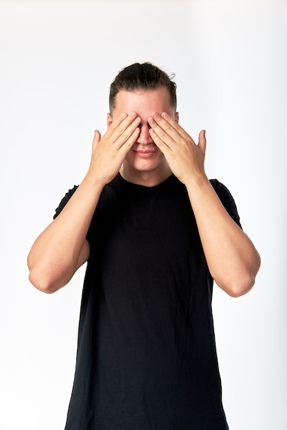 Young attractive man hiding his eyes by hands and smiling