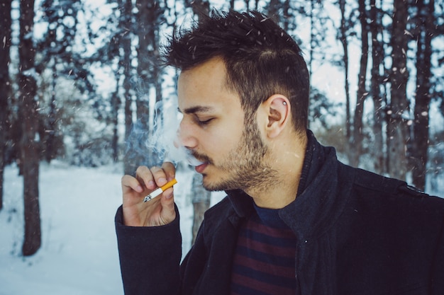 Young attractive man smoking  in forest during snow storm