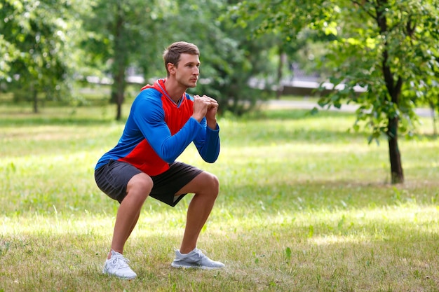 Young attractive man squatting outdoor in the park