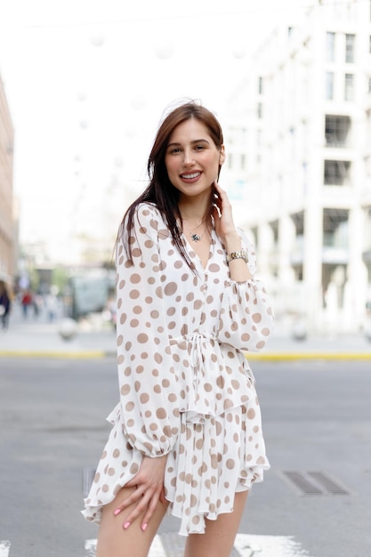 Young attractive pensive woman beautiful dress thoughtfully looking in camera standing on cozy city street