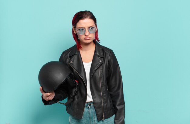 Young attractive red hair woman feeling sad, upset or angry and looking to the side with a negative attitude, frowning in disagreement. motorbike rider concept