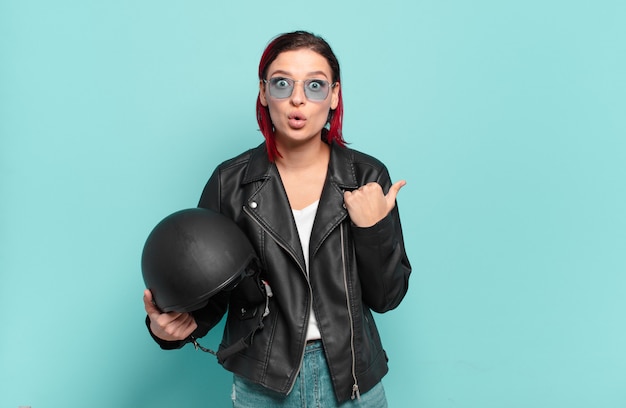 Young attractive red hair woman looking astonished in disbelief, pointing at object on the side and saying wow, unbelievable. motorbike rider concept