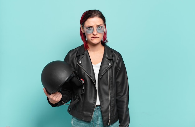 Young attractive red hair woman looking puzzled and confused, biting lip with a nervous gesture, not knowing the answer to the problem. motorbike rider concept