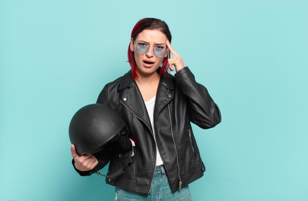 Young attractive red hair woman looking surprised, open-mouthed, shocked, realizing a new thought, idea or concept. motorbike rider concept