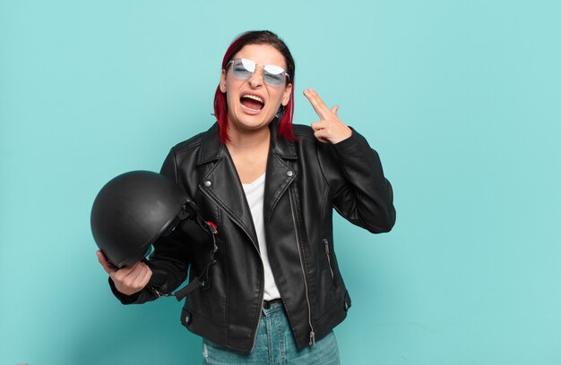 Young attractive red hair woman looking unhappy and stressed, suicide gesture making gun sign with hand, pointing to head. motorbike rider concept