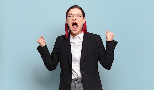 Young attractive red hair woman shouting aggressively with an angry expression or with fists clenched celebrating success