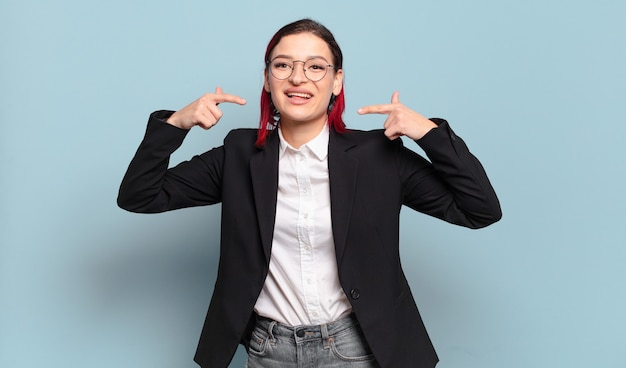 Young attractive red hair woman smiling confidently pointing to own broad smile, positive, relaxed, satisfied attitude