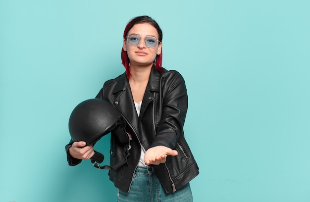 Young attractive red hair woman smiling happily with friendly, confident, positive look, offering and showing an object or concept. motorbike rider concept