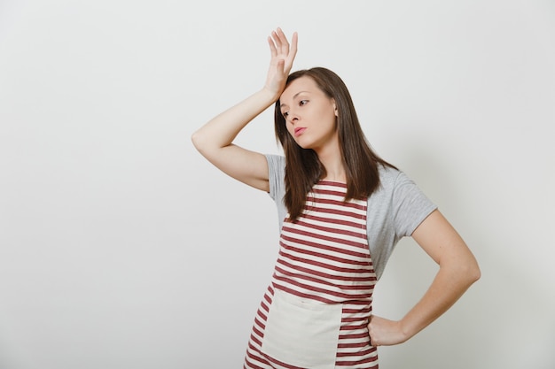 Young attractive sad upset tired brunette caucasian housewife in striped apron isolated. Beautiful housekeeper woman put and touch her hand to head