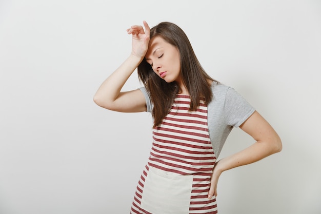 Young attractive sad upset tired brunette caucasian housewife in striped apron isolated. Beautiful housekeeper woman put and touch her hand to head