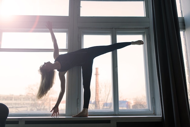 Young attractive smiling woman practicing yoga, working out, wearing sportswear, bra, home training