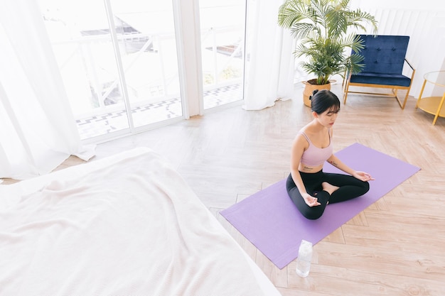 Young attractive sporty Asian woman practicing yoga on a yoga mat doing Ardha Padmasana exercise.