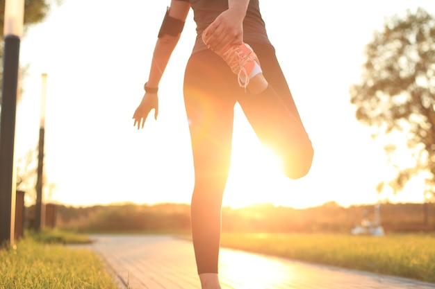 Young attractive sporty fitness woman runner warming up before run at sunset or sunrise on city