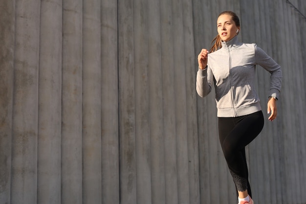 Young attractive sporty fitness woman running while exercising outdoors at sunset or sunrise in city.