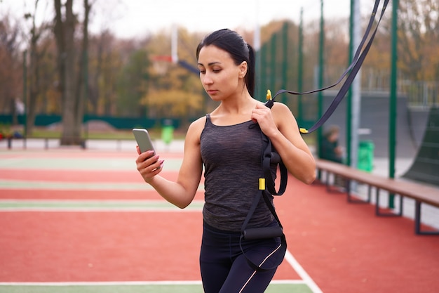 Young attractive woman does suspension training with fitness straps outdoors