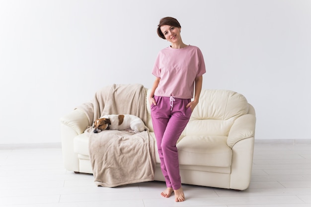 Young attractive woman dressed in beautiful colorful pajama posing with dog as a model in her living room. Comfortable sleepwear, home relaxation and female fashion concept.