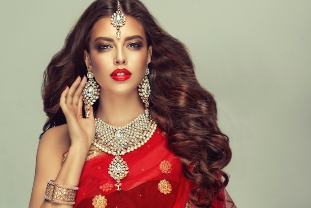 Young attractive woman, dressed in traditional indian red shawl (dupatta) and dressed in hand-made "kundan style" jewelry set.Perfect, dense, wavy, freely flying hair and "smoky eyes" style makeup.