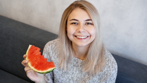 Young attractive woman eating watermelon. Woman at home in a cozy interior looking at camera and smiling