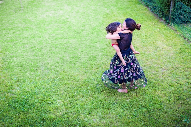 Young attractive woman holds her son in her arms and thay dance together in the backyard and laugh