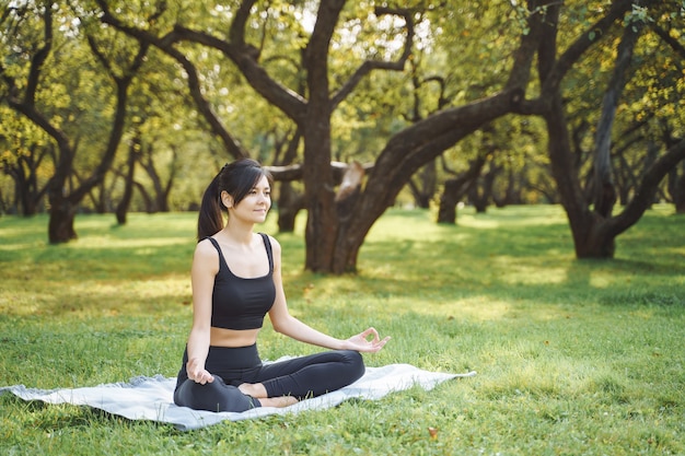 Young attractive woman meditating in lotus position sitting on the grass in the park.