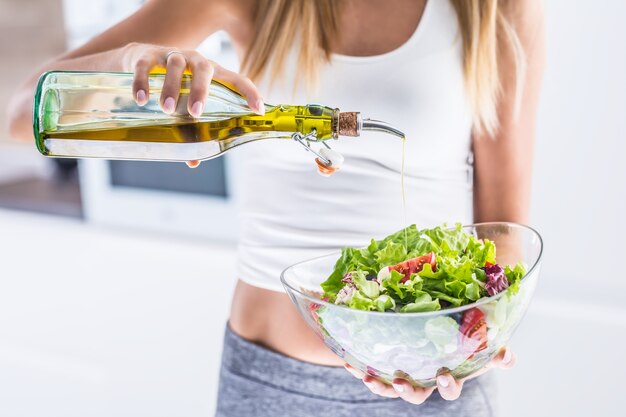 Young attractive woman pouring olive oil in to the fresh vegetable salad.