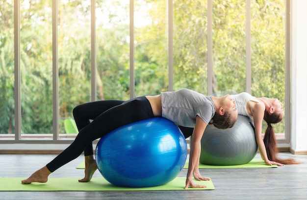 Young attractive woman practicing yoga working out with ball, wearing sportswear