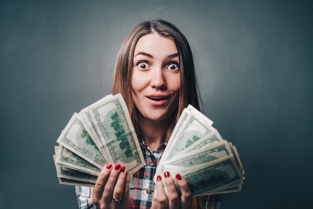 Young attractive woman showing sincere emotions of excitement and happiness with dollar banknotes in hands