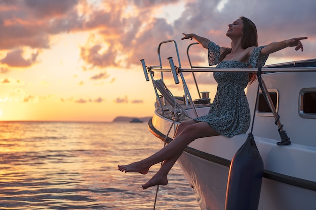 Young attractive woman sitting on the deck of yacht and enjoying sunset