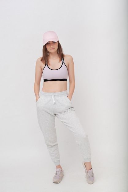 Young attractive woman in sporty suit and sneakers on white studio background. Sports studio portrait of brunette on white background.