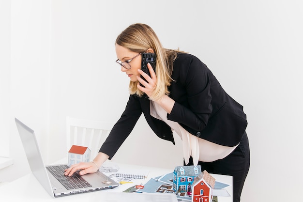 Young attractive woman talking on cellphone while working on laptop in real estate office