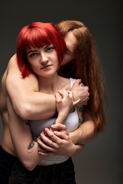 A young attractive woman with bright ruby hair in the arms of a seminaked man with long hair the lov