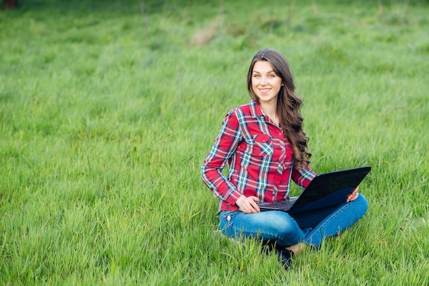 Young attractive woman with laptop on the grass in blooming garden